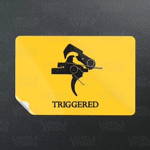 May include: A yellow sticker with a black silhouette of a gun trigger and the word "TRIGGERED" in black text.