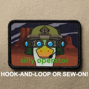 May include: A black and green embroidered patch featuring a cartoon duck wearing a military helmet and night vision goggles. The text "silly operator" is below the duck. The patch is designed for hook-and-loop or sew-on attachment.