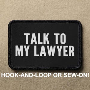 May include: Black patch with white text that reads "TALK TO MY LAWYER". The patch is sewn with black thread and has a hook-and-loop or sew-on option.