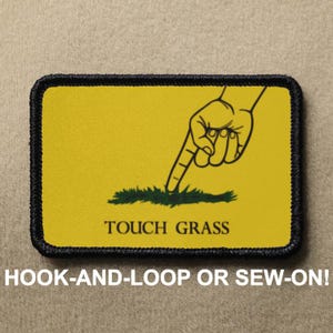 May include: Yellow patch with a black border and a black hand pointing down to green grass. The text "TOUCH GRASS" is below the hand. The patch is for hook-and-loop or sew-on.
