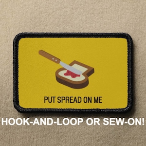 以下が含まれることがあります： 黒い縁取りのある黄色のパッチには、ナイフがトーストにジャムを塗っているという漫画の画像が描かれています。画像の下には「PUT SPREAD ON ME」というテキストが印刷されています。このパッチは、面ファスナーで取り付けたり、縫い付けたりするように設計されています。