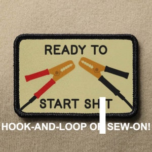 May include: A beige patch with black stitching around the edges. The patch features a graphic of two jumper cables with the text "READY TO START SH T" in black. The text "HOOK-AND-LOOP OR SEW-ON!" is printed below the graphic.