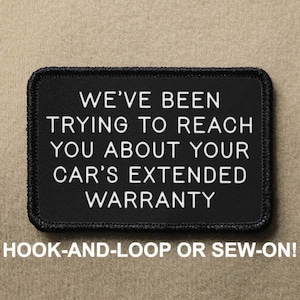 Op de afbeelding: Een zwart rechthoekig embleem met witte tekst die luidt: "WE'VE BEEN TRYING TO REACH YOU ABOUT YOUR CAR'S EXTENDED WARRANTY." De tekst "HOOK-AND-LOOP OR SEW-ON!" staat eronder. Het embleem heeft een zwarte rand.