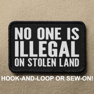 May include: Black and white patch with the text "NO ONE IS ILLEGAL ON STOLEN LAND". The patch is designed to be attached with hook-and-loop or sewn on.