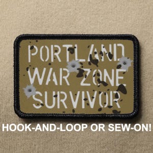 Puede incluir: Parche rectangular con el texto "PORTLAND WAR ZONE SURVIVOR" en blanco, con gráficos de agujeros de bala. El parche tiene un borde negro y el texto "HOOK-AND-LOOP OR SEW-ON!" en la parte inferior.