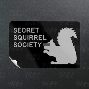 Könnte beinhalten: Schwarz-weißer Aufkleber mit dem Text "SECRET SQUIRREL SOCIETY" und einer Silhouette eines Eichhörnchens. Der Aufkleber hat einen weißen Rand und der Text "LUMOLA STUDIO" ist auf dem Aufkleber gedruckt.