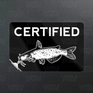 May include: Black and white sticker with the text "CERTIFIED" and a drawing of a catfish. The sticker has the text "LUMOLA STUDIO" repeated around the border.