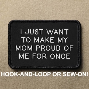 May include: Black and white embroidered patch with the text "I JUST WANT TO MAKE MY MOM PROUD OF ME FOR ONCE". The patch is attached to a brown fabric background. The text is in a white sans-serif font. The patch is available in hook-and-loop or sew-on options.