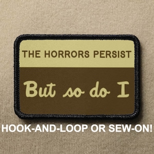 May include: A brown and beige patch with black stitching around the edges. The patch has the text "THE HORRORS PERSIST" in white on a beige background. Below that, the text "But so do I" is in white on a brown background. The patch is labeled "HOOK-AND-LOOP OR SEW-ON!"