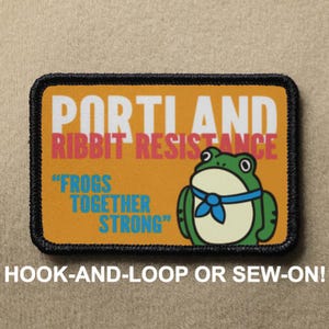 Puede incluir: Parche rectangular con borde negro y fondo naranja. El parche presenta el texto "PORTLAND RIBBIT RESISTANCE" y "FROGS TOGETHER STRONG". Una rana de dibujos animados con una pajarita azul está a la derecha.