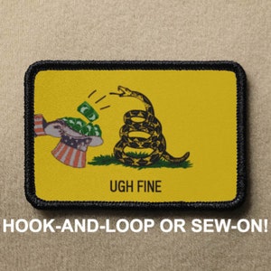 May include: A yellow patch with a black border features a green snake with a coiled body and a raised head. The snake is holding a stack of green dollar bills in its mouth. The text "UGH FINE" is printed below the snake. The patch is designed for hook-and-loop or sew-on attachment.