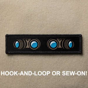 May include: Black rectangular patch with a binoculars design in brown and blue. The text "HOOK-AND-LOOP OR SEW-ON!" is printed in white below the binoculars graphic. The patch is designed for easy attachment to clothing or bags.