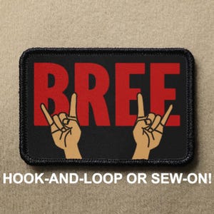 Pode incluir: Patch preto com texto vermelho que diz "BREE" com duas mãos de desenho animado fazendo o gesto de rock and roll.