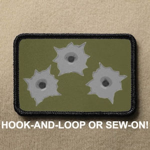 May include: Green fabric patch with three gray bullet holes. The patch has black stitching around the edges and says "HOOK-AND-LOOP OR SEW-ON!" at the bottom.