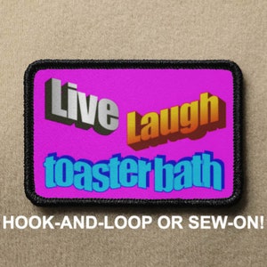 May include: A pink and black patch with the text "Live Laugh Toasterbath" in colourful, 3D-style lettering. The patch is designed to be attached with hook-and-loop or sewn on.