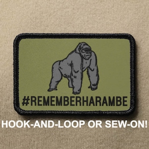Puede incluir: Un parche bordado verde y negro con una ilustración en blanco y negro de un gorila y el texto "#REMEMBERHARAMBE". El parche es para sujetar con velcro o coser.