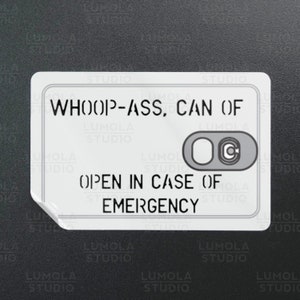 May include: White sticker with the text "WHOOP-ASS, CAN OF" and "OPEN IN CASE OF EMERGENCY". The sticker has a small, round, gray toggle switch with a "C" printed on it.