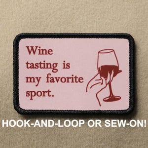 Puede incluir: Un parche bordado rosa y negro con el texto "Wine tasting is my favorite sport." y una copa de vino tinto con una mano sujetando el tallo. El texto "HOOK-AND-LOOP OR SEW-ON!" está impreso debajo del parche.