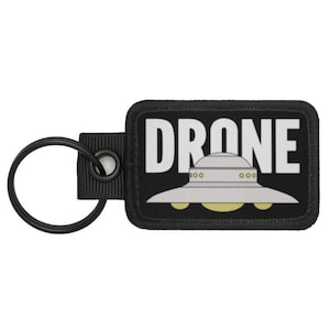 May include: Black key chain with a black and white patch that says "DRONE" with a cartoon UFO underneath.