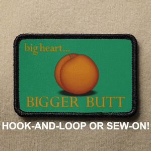 Peut inclure: Un patch brodé vert et noir avec le texte "big heart... BIGGER BUTT" et une illustration de pêche.