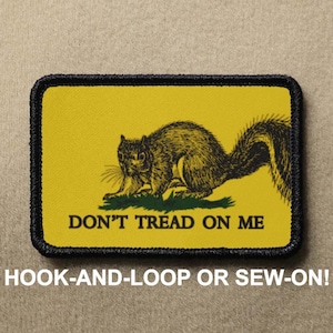 Könnte beinhalten: Ein gelber Patch mit schwarzem Rand und einem Schwarzweißbild eines Eichhörnchens mit dem Text "Don't Tread On Me". Der Patch ist mit "Hook-and-Loop or Sew-On!" beschriftet.