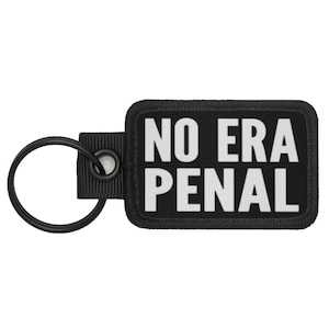 May include: A rectangular black embroidered keychain featuring the white text NO ERA PENAL in a bold sans-serif font. The keychain includes a black fabric tab and a circular black metal split ring attached to the left side of the patch.