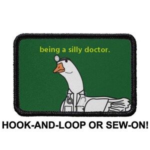 Puede incluir: Un parche bordado verde y negro con un ganso blanco que lleva un estetoscopio y un gorro de médico. El texto "being a silly doctor." está escrito en amarillo en el parche. El parche está etiquetado como "HOOK-AND-LOOP OR SEW-ON!"