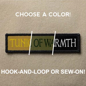 Könnte beinhalten: Ein schwarzer, grüner und gelber Patch mit dem Text "TUNIC OF WARMTH" in weißen Buchstaben. Der Patch ist in Klett- oder Nähvariante erhältlich.