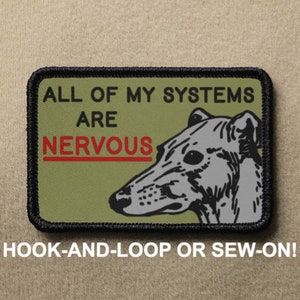 Op de afbeelding: Rechthoekige patch in olijfgroen met de tekst "ALL OF MY SYSTEMS ARE NERVOUS" in zwart en rood. Een illustratie van een windhond staat rechts. De patch heeft een zwarte rand. De tekst "HOOK-AND-LOOP OR SEW-ON!" staat onderaan.