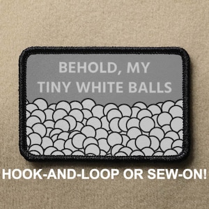 Peut inclure: Un écusson brodé gris et noir avec le texte "BEHOLD, MY TINY WHITE BALLS" et un motif de cercles blancs sur un fond gris. L'écusson a une bordure noire et indique "HOOK-AND-LOOP OR SEW-ON!" en bas.