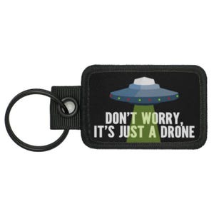 May include: Black key chain with a black and green patch that says "Don't worry, it's just a drone." The patch features a cartoon UFO with green lights.