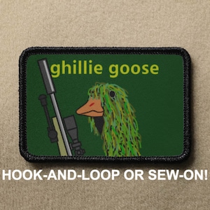 Peut inclure: Un patch brodé vert et noir avec une oie de dessin animé portant un camouflage et tenant un fusil de sniper. Le texte "ghillie goose" est écrit en jaune au-dessus de l'oie. Le patch a une bordure noire et dit "HOOK-AND-LOOP OR SEW-ON!" en dessous de l'image.