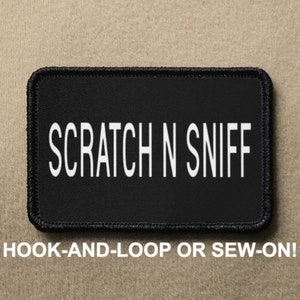 May include: Black patch with white text that reads "SCRATCH N SNIFF". The patch is for hook-and-loop or sew-on attachment.