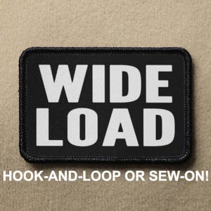 May include: Black patch with white text that reads "WIDE LOAD". The patch is for hook-and-loop or sew-on attachment.