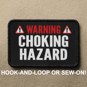 Könnte beinhalten: Schwarzer Patch mit weißem Text, der "WARNING CHOKING HAZARD" lautet, mit einem roten Ausrufezeichen auf jeder Seite. Der Patch hat schwarze Nähte an den Rändern und ist so konzipiert, dass er mit Klettverschluss befestigt oder angenäht werden kann.