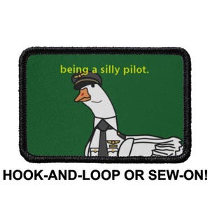 Könnte beinhalten: Gestickter Aufnäher mit einer Comic-Gans in Pilotenuniform, mit dem Text "being a silly pilot." Der Aufnäher hat einen grünen Hintergrund und einen schwarzen Rand. Der Text "HOOK-AND-LOOP OR SEW-ON!" steht darunter.