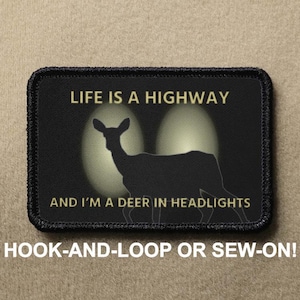 May include: Black and white patch with the text "LIFE IS A HIGHWAY AND I'M A DEER IN HEADLIGHTS". A silhouette of a deer is in the center of the patch. The patch is surrounded by a black border.