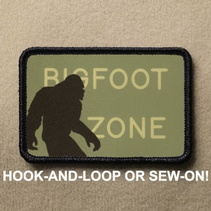 May include: A green and black patch featuring a silhouette of Bigfoot walking and the text "BIGFOOT ZONE". The patch is designed for hook-and-loop or sew-on attachment.