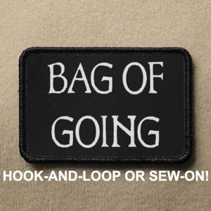 Könnte beinhalten: Schwarzer Patch mit weißem Text, der "BAG OF GOING" lautet. Der Patch hat einen schwarzen Rand und ist zum Annähen oder Anbringen an Kleidung gedacht.