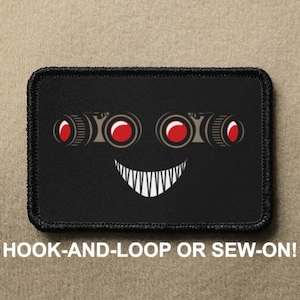May include: Black patch with a white stitched border. The patch features a cartoon face with red eyes and a wide, toothy grin. The text "HOOK-AND-LOOP OR SEW-ON!" is printed below the patch.