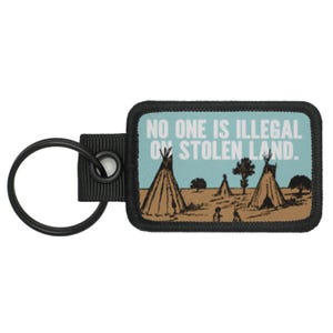 Pode incluir: Chaveiro preto com um gráfico preto e branco de tipis e o texto "No one is illegal on stolen land."