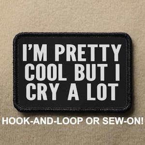 May include: Black and white embroidered patch with the text "I'M PRETTY COOL BUT I CRY A LOT". The patch is attached to a brown fabric background. The patch can be attached with hook and loop or sewn on.