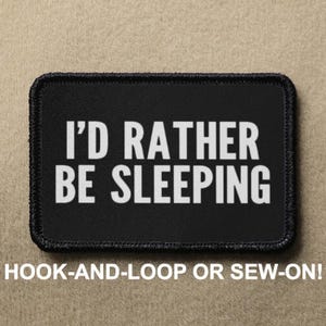 Peut inclure: Écusson noir avec du texte blanc qui dit "I'd rather be sleeping". L'écusson est conçu pour être fixé par scratch ou cousu.