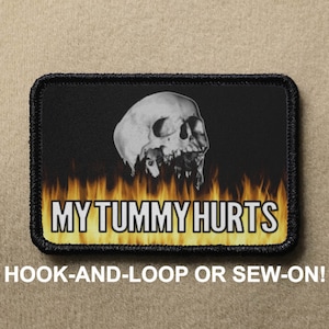 May include: Black and white skull with flames behind it, on a black patch with white text that says "MY TUMMY HURTS". The patch has black stitching around the edges.