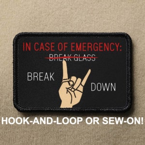 Pode incluir: Patch preto com texto branco que diz "EM CASO DE EMERGÊNCIA: QUEBRE O VIDRO" com uma linha vermelha atravessando "QUEBRE O VIDRO". Abaixo do texto, há uma mão branca fazendo o gesto de "rock on" com o texto "BREAK" à esquerda e "DOWN" à direita. O patch tem costuras pretas ao redor das bordas. O texto "HOOK-AND-LOOP OR SEW-ON!" está escrito em branco abaixo do patch.
