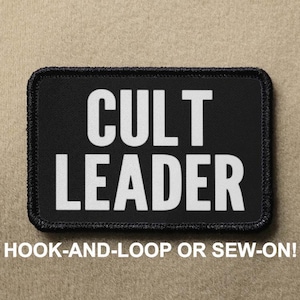 May include: Black rectangular patch with white text that reads "CULT LEADER." The patch has a black border and the text "HOOK-AND-LOOP OR SEW-ON!" below the main text.