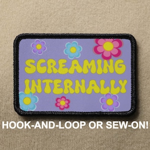 May include: Purple patch with a black border and a white background. The patch has a yellow text that says "Screaming Internally" with a flower pattern in pink, yellow, and blue.