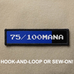 Könnte beinhalten: Blauer und schwarzer gestickter Aufnäher mit weißem Text, der "75/100 MANA" lautet.