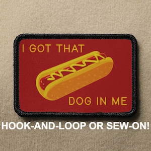 Peut inclure: Un patch brodé rouge et noir avec un hot-dog et le texte "I got that dog in me". Le patch a un dos à scratch.