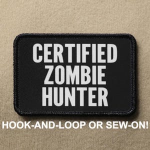 Puede incluir: Parche negro con texto blanco que dice "CERTIFIED ZOMBIE HUNTER". El parche tiene un borde negro y está diseñado para ser fijado con velcro o cosido.